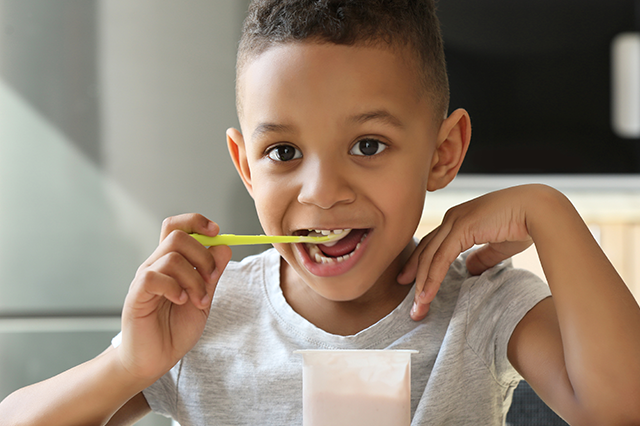 A young boy enjoys some yogurt as a soft food to eat after dental work