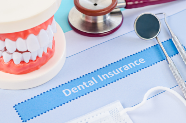 The word Dental Insurance written on a piece of paper, on a desk surrounded by false teeth and dental instruments