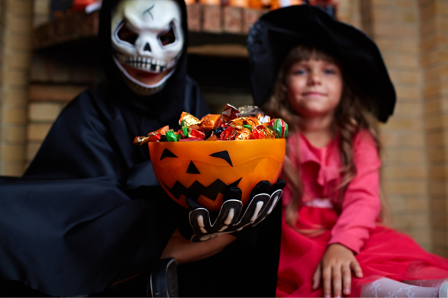 Two kids in halloween costumes holding a bowl of halloween candy 
