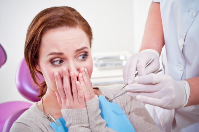 A woman sitting in a dentist chair covering her mouth with fear