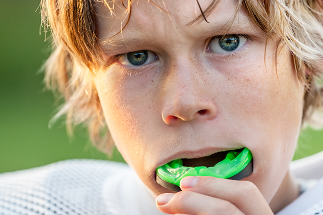 a young football player is inserting his sports mouthguard before play begins